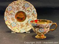 Photo of vintage teacup and matching saucer with blue floral chintz pattern and gold inlay detail, displayed on black background.
