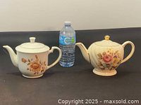 Two vintage ceramic teapots next to a water bottle for scale on black cloth background.