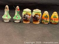 Photo showing full set of three pairs of vintage porcelain salt and pepper shakers with varying hand-painted designs on black background