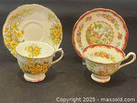 Two teacups and two saucers, one set with yellow floral design and the other with a red border and bird motif.