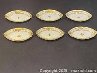 Six oval antique Moriage Nippon nuts dishes displayed on black background, showing uniform size, hand-painted floral decoration, and gold rims.