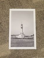Black and white photo print showing Alexandria Lighthouse in Egypt, centered in portrait orientation with visible white border on all sides, placed over a textured carpet surface.