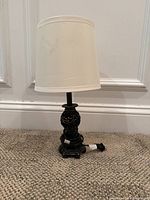 Full view of the black resin table lamp showing the white fabric lampshade and ornamental scrollwork base accented in gold.