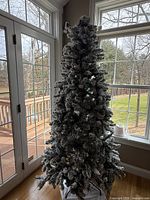 Full view of the 7-foot artificial Christmas tree with frosted branches set up indoors by window