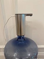 Front view of silver electric water dispenser mounted on a large blue water jug, showing spout and power cord.