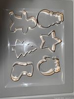 Photo showing 8 cookie cutters including gingerbread man, Christmas tree, bell, boot, star, crescent, cloud and triangle shapes.