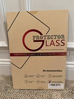 Front of the beige packaging for the tempered glass screen protector with text describing six characteristics including oleophobic coating and tempered glass.