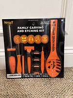 Front view of the Spirit Halloween Family Carving and Etching Kit box showing included carving tools, stencils, and scoop in orange and black packaging.