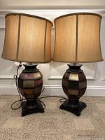 Pair of patchwork design table lamps with beige fabric shades shown side by side on carpeted floor against white wall paneling.