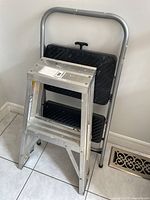 Aluminum foldable step stool folded standing upright showing slip-resistant black steps and aluminum frame.