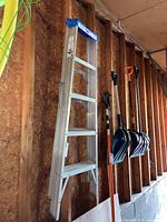 Full image of 5-foot aluminum ladder hanging on wooden wall showing structure and adjacent tools.