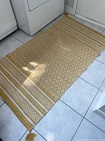 Top view of full rectangular area rug showing geometric patterns and yellow-white color scheme placed on a tiled floor.