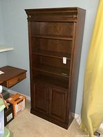 Full front view of the wooden bookshelf showing two open shelves and closed bottom cabinet with double doors.