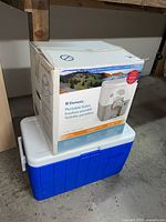 Dometic portable toilet box stacked on Coleman cooler in basement setting.
