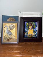 Two framed prints set on floor, one with bird decoupage on left and colorful abstract figure print on the right