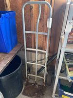 Full view of upright metal dolly showing frame and base plate with rust