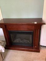 Front view of electric fireplace showing wooden mantel with two columns and black firebox with simulated logs inside.