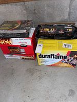 Two boxes of fire logs (Duraflame and Zip) stacked next to an unopened Instant Light BBQ grill box in a garage setting.