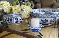 Photo of the square blue and white porcelain flower pot with artificial white flowers and large shell-themed bowl on the glass table