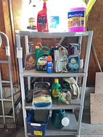 Four-tier resin shelf filled with assorted garden and household supply bottles and containers, including weed control, insect sprays, absorbent towels, plant food, watering can, pail, and car products.