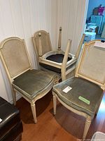 Four chairs with antique finish wood frames, cane backs, olive-green upholstered seats; one chair shown upside down