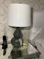 Photo of one porcelain table lamp showing glossy gray body, white fabric shade, clear round base, and finial on top.