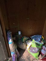 Lots of lawn and garden items including green tomato cages, burlap rolls, bags of soil, pellet, seeds, and a large clay urn.