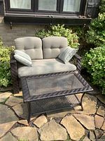 Full view of loveseat and table on stone patio amid greenery
