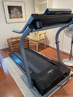 Side angled photo of NordicTrack EXP1000 treadmill showing cushioned track, handrails, and console.