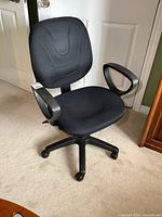 Front view of the black office chair showing cushioned backrest, seat, armrests, and wheeled base.