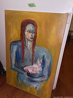 Full view of the mounted oil painting showing a blue-skinned woman with red hair holding a pink rabbit, set against a yellow ochre background.