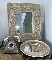 Photo showing the Bombay Classic Tiffany Retro model brushed metal finish push button phone in front of square carved floral frame mirror and round textured frame mirror.