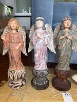Front view of all three resin angel figurines standing on a rug in front of furniture.