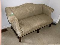 Full view of beige floral damask sofa showing curved back and wooden base.