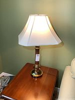 Full view of the vintage table lamp on wooden table against a green wall showing the white fabric shade lit.