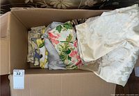 Top view of box containing folded table cloths and place mats with various floral patterns and colors.