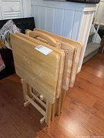 Four solid wood TV trays in the matching wooden stand placed on hardwood flooring.