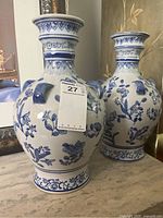 Pair of large blue and white chinoiserie style ceramic vases with floral and leaf motifs, three blue sculptural loop handles each, displayed on a table.