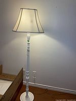 Full view of the floor lamp lit with fabric shade on and white painted wooden base and post.