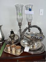 Collection of vintage silver plated items including candle holders with hurricane shades, serving trays, small candle holders, and a creamer pitcher.