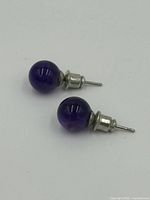 Close-up front view of the two amethyst stud earrings showing deep purple spherical stones and silver-tone stud posts with backs.