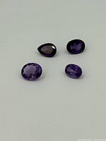 Four loose amethyst gemstones on a white background showing color and cut variety