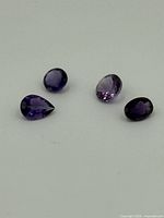 Four loose amethyst gemstones laid on white background showing color and shape variations.