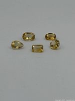 Five citrine gemstones displayed on white surface showing various cuts and yellow hues.