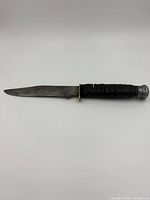 Side view of cutter knife showing blade and textured handle with metal pommel.