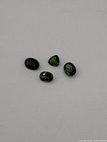 Four Demantoid Garnet stones on white background showing overall color and shape variety