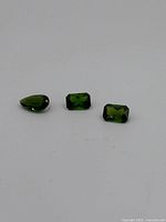 Three green dermatoid garnet gemstones displayed on white background.