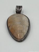 Front view of fossilized coral pendant showing smooth polished fossil stone with floral pattern inside a tarnished sterling silver bezel.