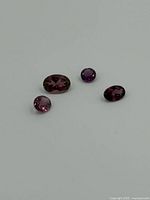 Four oval garnet gemstones in dark reddish and purplish shades arranged on a flat white surface.