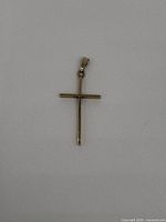 Top view of a small, thin 10kt gold cross pendant on white background.
